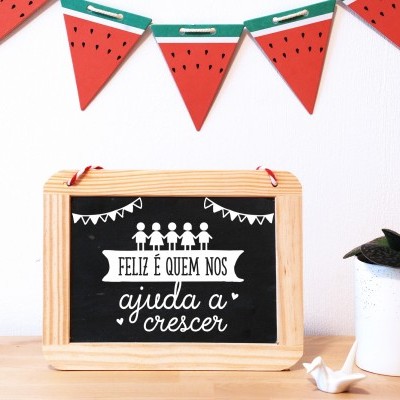 Quadro negro com moldura de madeira, frase motivacional em português, vaso branco e guirlanda de melancia na parede branca