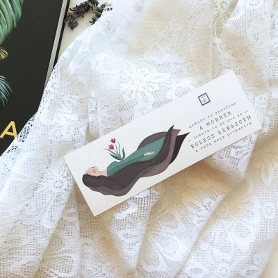 Etiqueta branca com ilustração e texto sobre tecido de renda branco ao lado de revista