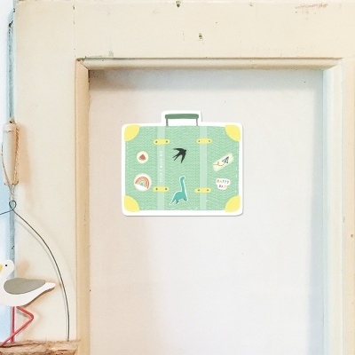 Mala decorativa verde com desenhos de animais pendurada numa porta branca, com decoração de pássaro ao lado