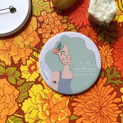 Botão redondo com ilustração feminina e texto inspirador em fundo floral colorido