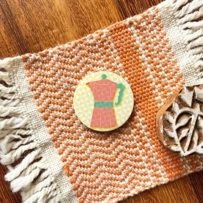 Dois objetos sobre tecido artesanal laranja e branco com franjas sobre madeira