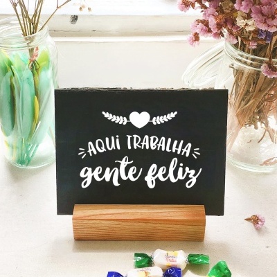 Cartaz preto com texto branco sobre base de madeira e frascos de vidro com flores e decoração