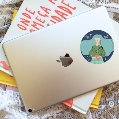 Tablet prateado Apple com autocolante ilustrado, em cima de dois livros sobre tecido rendado branco