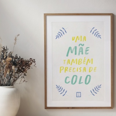 Poster emoldurado com texto colorido e um vaso branco com flores secas numa parede branca
