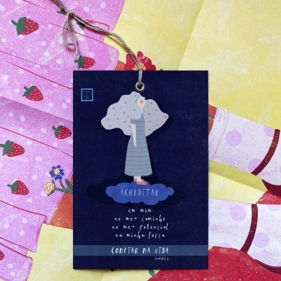 Etiqueta pendurada azul com texto em português sobre fundo colorido com padrão de morangos e bolas cor-de-rosa