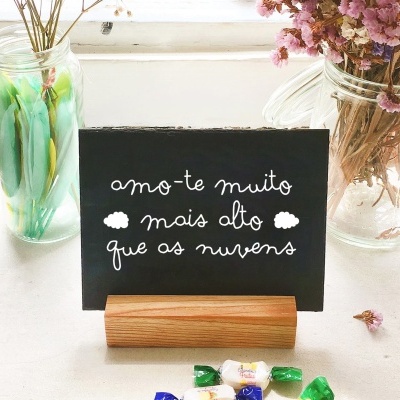 Placa preta com texto em letra branca em suporte de madeira entre frascos com flores secas