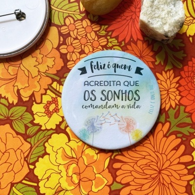 Dois crachás redondos com texto e ilustrações sobre padrão floral colorido com pedra e noz ao lado.