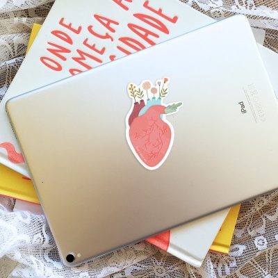 iPad prateado com autocolante de coração e livros com frase em português sobre renda branca