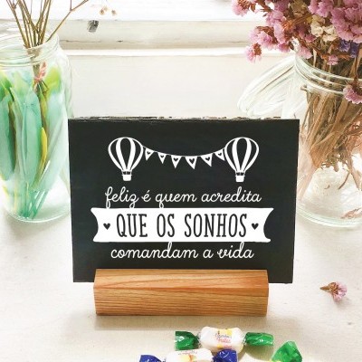 Postal motivacional sobre suporte de madeira num ambiente com frascos de vidro e doces