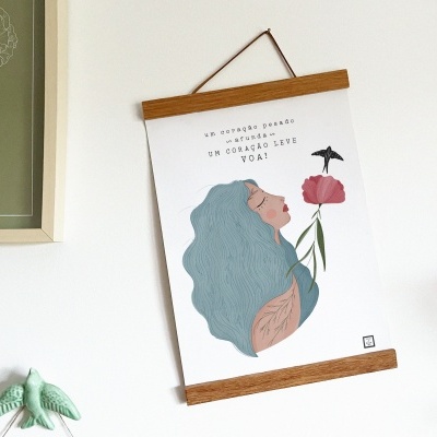 Poster ilustrado com mulher de cabelo azul e flor rosa pendurado na parede com moldura de madeira clara