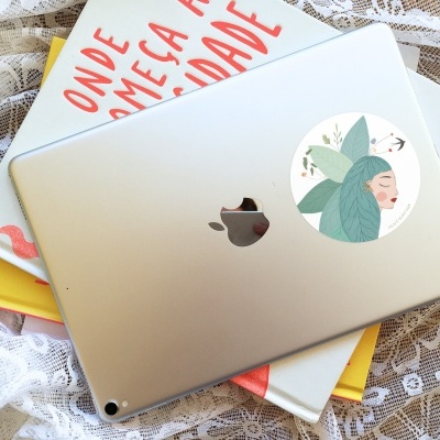 Tablet prateado com autocolante de mulher de cabelo folhas, sobre livros e tecido rendado branco.