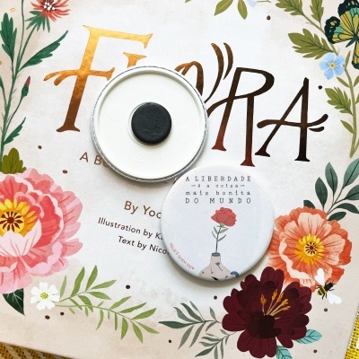 Botões redondos com ilustração, sobre livro com capa floral e título Flora