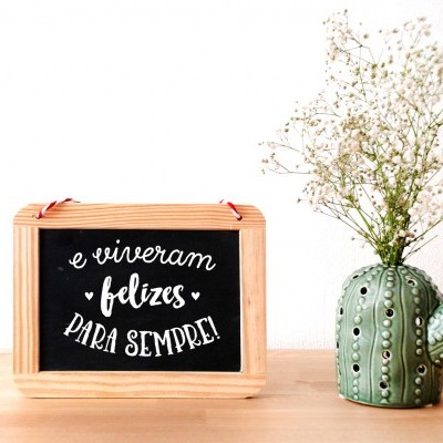 Placa decorativa com texto e jarra em forma de cacto com flores secas num fundo claro