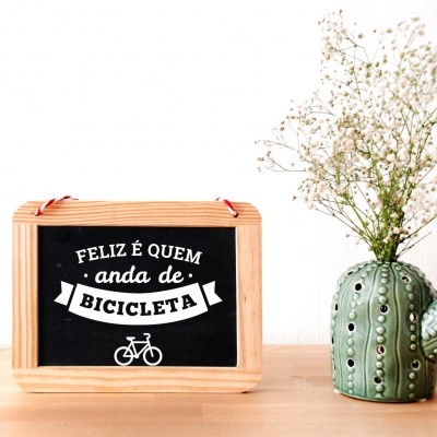 Quadro com mensagem sobre bicicleta ao lado de vaso em forma de cacto com flores.