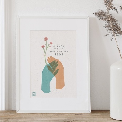 Quadro decorativo com mãos e flor e texto 'O AMOR NASCE DE UMA FLOR' ao lado de jarro com ramos secos