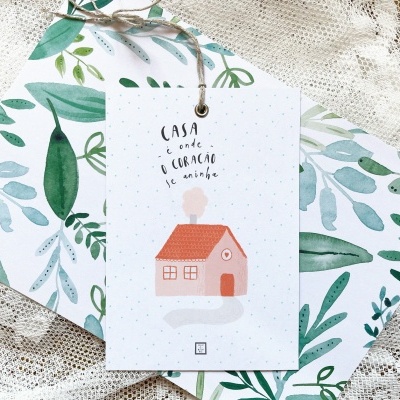 Cartão com ilustração de casa cor-de-rosa e texto, sobre cadernos com padrão de folhas verdes