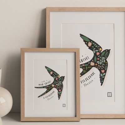 Dois quadros decorativos com andorinhas coloridas, molduras de madeira e um vaso cinzento ao lado