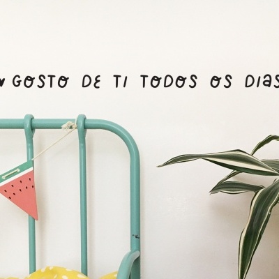 Cama metálica verde, guirlanda de melancia, planta em vaso, parede branca com texto em português.