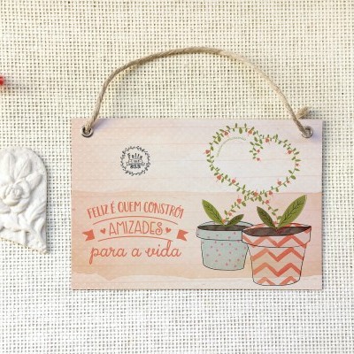 Placa decorativa em madeira com texto e vasos pintados, e coração decorativo branco pendurado