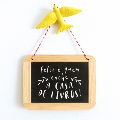 pequeno quadro negro com moldura de madeira clara e corda para pendurar com pássaro amarelo e texto em branco