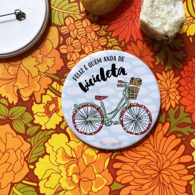 Pin redondo branco com bicicleta e texto em cima de padrão floral colorido