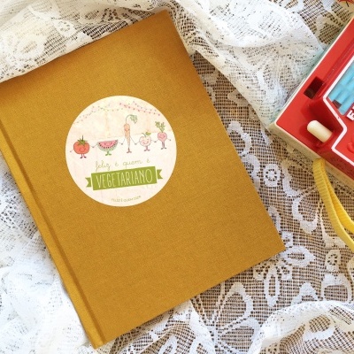 Livro amarelo com etiqueta vegetariana e máquina fotográfica Fisher-Price vermelha sobre renda branca