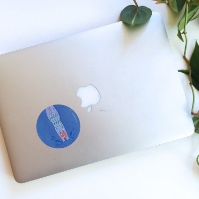 Portátil Apple prateado com autocolante azul e folhas verdes ao lado