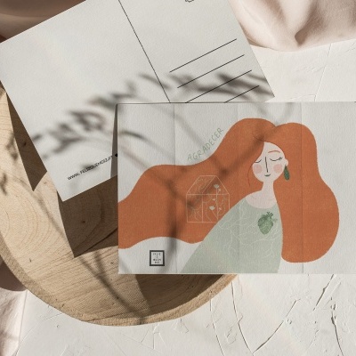 Dois postais, um com ilustração de mulher de cabelo ruivo e outro com verso para correspondência, sobre superfície branca texturizada