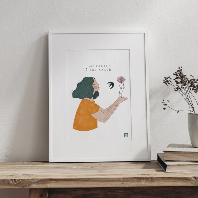 quadro branco com ilustração de mulher e texto, sobre móvel de madeira com vaso e livros