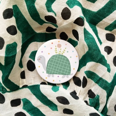 Botão branco com tartaruga sobre tecido branco com riscas verdes e manchas pretas
