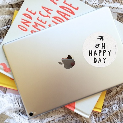 Tablet prateado com autocolante OH HAPPY DAY sobre livros e renda branca.