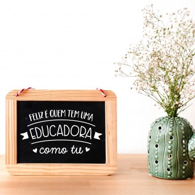 Quadro negro com frase e vaso de cerâmica em formato de cacto com flores sobre mesa de madeira