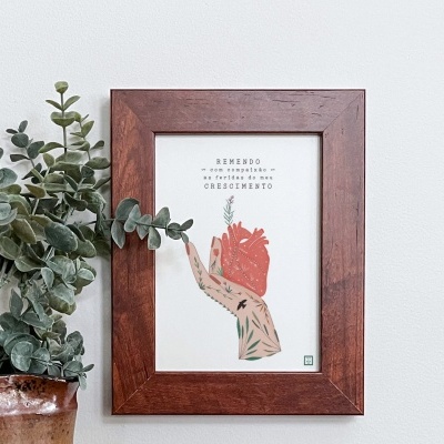 Quadro emoldurado com ilustração e texto, ao lado de vaso com planta