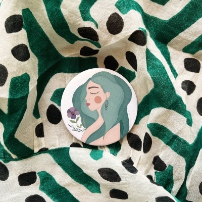 Botão redondo com ilustração de mulher segurando flor sobre tecido verde, branco e preto