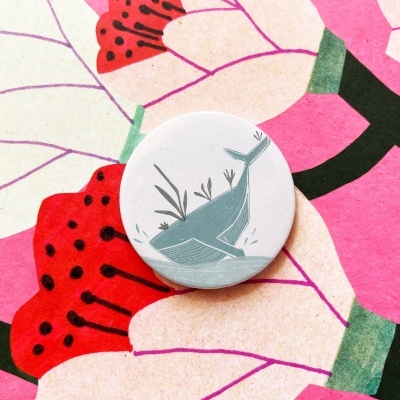 Botão branco com desenho de baleia sobre padrão de flores rosa e vermelhas