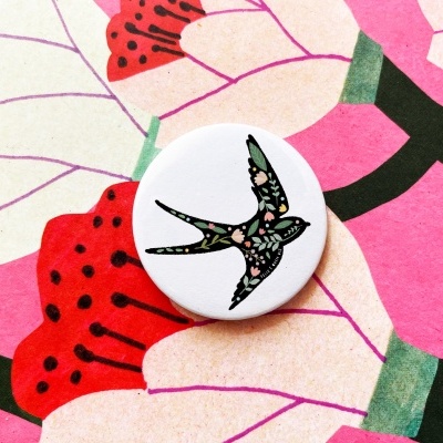 Botton branco com desenho de andorinha colorida sobre fundo floral colorido