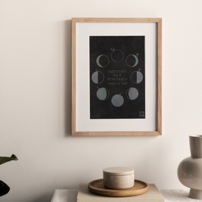 Quadro com fases da lua numa parede branca e objetos decorativos em cima de uma superfície