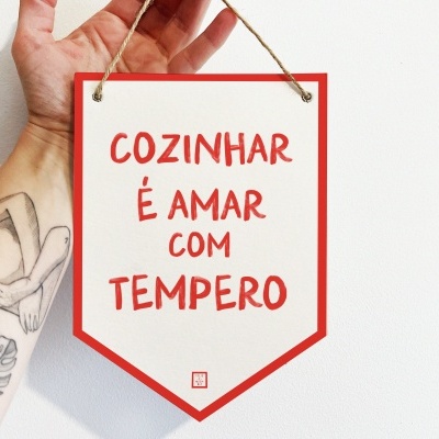 Placa decorativa com texto 'COZINHAR É AMAR COM TEMPERO' em fundo branco e borda vermelha