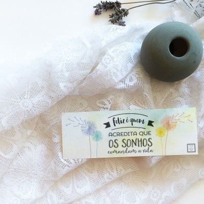 Vela branca com texto inspirador, vaso verde e raminhos secos sobre tecido rendado branco