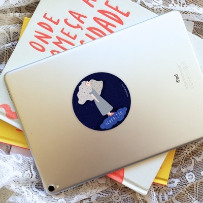 iPad prateado com autocolante azul, sobre livros com capa branca e letras vermelhas, fundo de renda branca