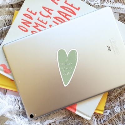 iPad prateado com autocolante em forma de coração sobre livros com capas branca, vermelha e amarela, em fundo de renda branca