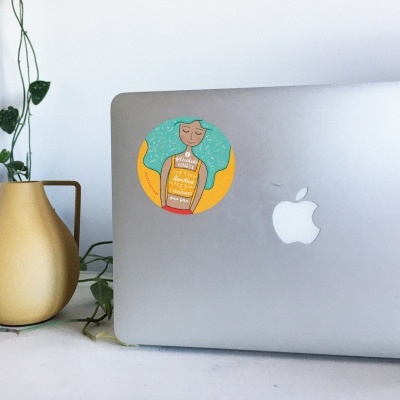 Computador portátil prateado com autocolante colorido de mulher com cabelo azul e vaso amarelo com plantas em fundo branco