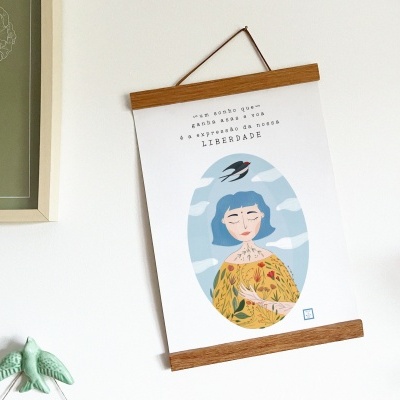 Cartaz pendurado com ilustração de mulher e pássaro, texto em português e moldura de madeira