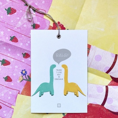 Etiqueta com ilustração de dinossauros pendurada sobre tecido com padrão de morangos e tecido amarelo com manchas