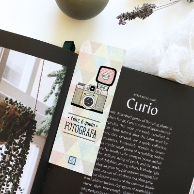 Marcador de página colorido com máquina fotográfica e livro aberto com texto em inglês sobre fundo branco.