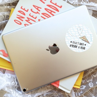 Computador portátil prateado Apple com autocolante, apoiado em livros sobre renda branca