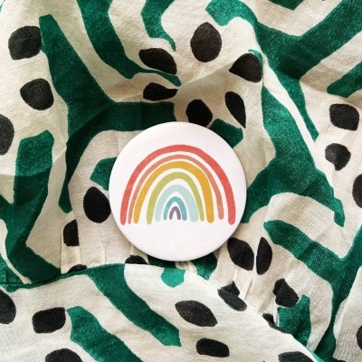 Broche redondo com arco-íris sobre tecido com padrão verde escuro e preto