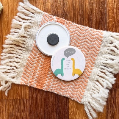 Ímans redondos de dinossauros sobre manta laranja com franjas em mesa de madeira