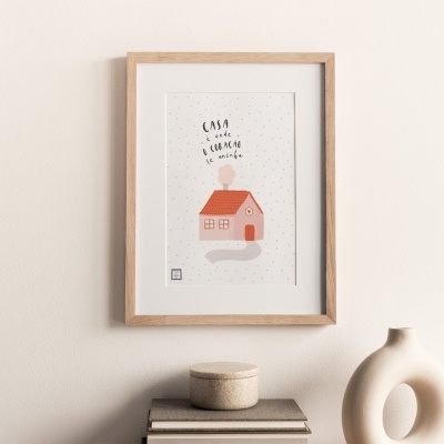 Quadro decorativo com moldura de madeira e ilustração de casa com texto na parede, acima de livros e objetos decorativos.