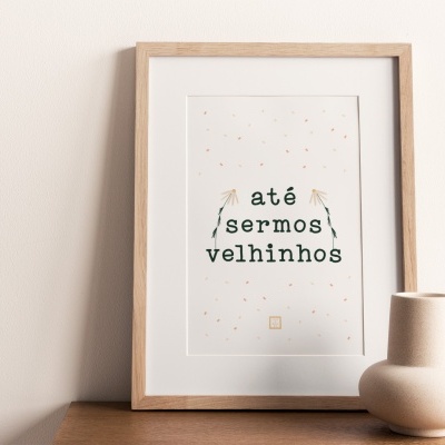 Quadro com frase 'até sermos velhinhos' em moldura de madeira com vasos decorativos ao lado